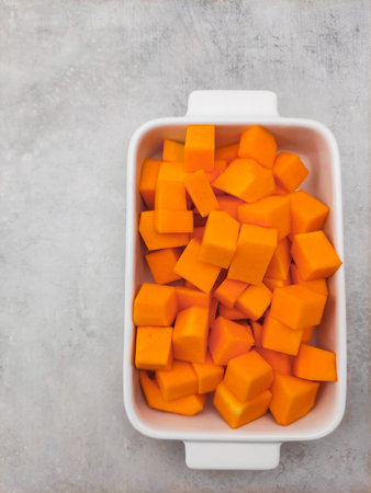 Freshly cut butternut squash cubes are neatly arranged in a white ceramic baking dish, ready for roastingの写真素材