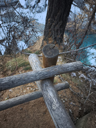 Weathered wooden fence bordering turquoise river valley, alpine landscape with snow capped mountains in valle d'aosta, italy Cascate di Lillazの写真素材