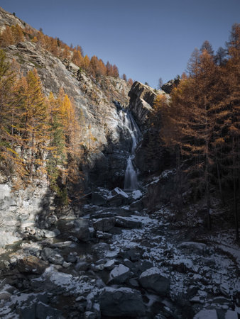 Stunning waterfall flows through rocky cliffs surrounded by autumn foliage in Aosta, Italy, capturing the serene beauty of nature in november Cascate di Lillazの写真素材