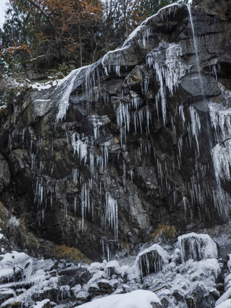 Icicles hang from a rugged cliff in aosta, italy, showcasing nature's winter artistry with cascading...