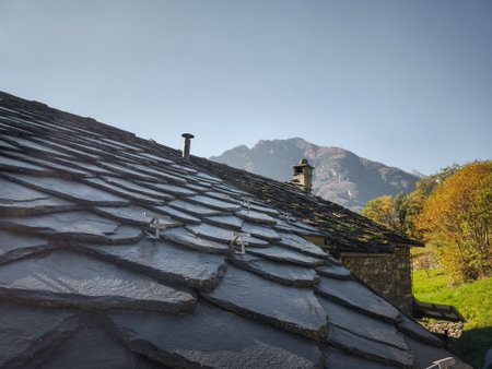 Slate roof of a rustic building in Aosta, Italy, with majestic mountains and autumn foliage in the background, capturing a serene november landscape Verresの写真素材