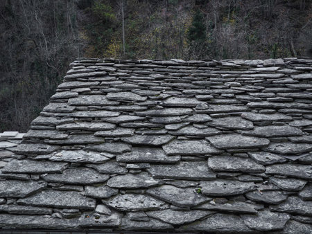 Weathered stone roof with rugged texture set against a backdrop of aosta's november foliage,...