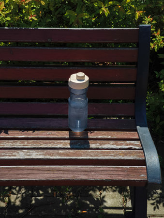 Reusable water bottle sitting on park bench promoting hydration and sustainabilityの写真素材