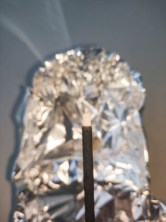 Incense stick burning with aluminum foil in the background