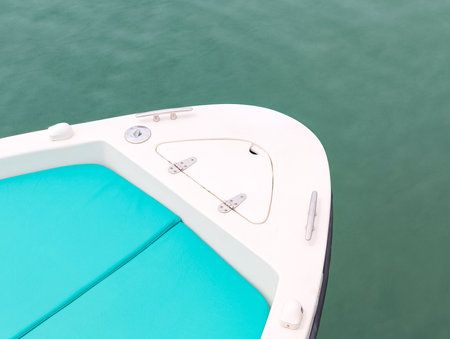 Close up of the bow of a white motorboat featuring turquoise cushions, metal fittings, and a small hatch, peacefully floating on tranquil green waterの写真素材