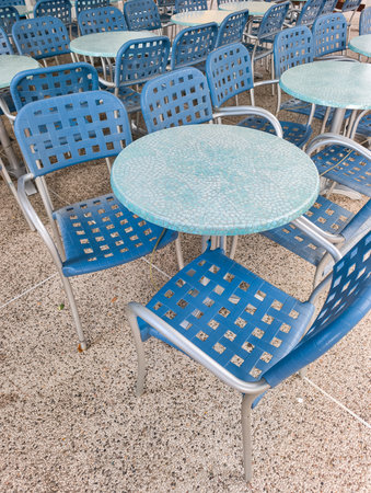 Numerous blue chairs are surrounding light blue round tables in an outdoor cafe in lignano sabbiadoro, creating a relaxing and inviting atmosphereの写真素材