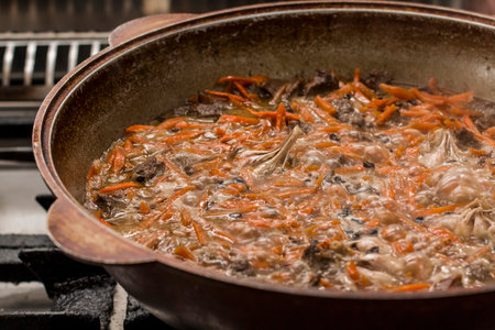 A large pot filled with a traditional Uzbek dish, pilaf, simmering with tender meat and vibrant carrots, creating a warm and inviting atmosphere in a rustic kitchenの写真素材