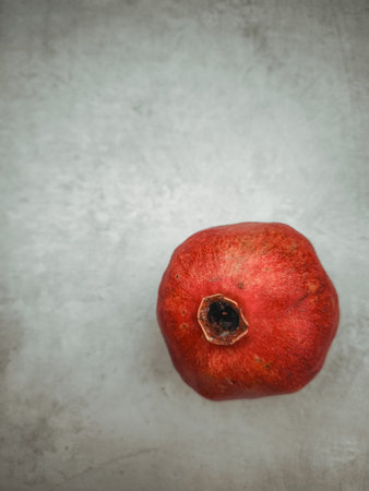 Ripe pomegranate resting on a textured, neutral toned surface, representing the symbolism of rosh hashanah, rebirth, love, and abundance across culturesの写真素材
