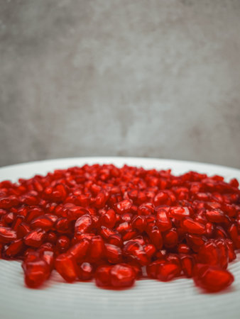 Overflowing pomegranate seeds on a white plate create a vibrant display of red against a muted background, symbolizing abundance, rebirth, and love across culturesの写真素材