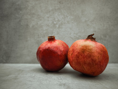 Two ripe pomegranates rest on a gray surface, embodying the themes of love, rebirth, and abundance associated with rosh hashanah and Greek mythology, against a textured gray backgroundの写真素材