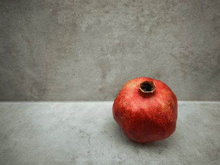 Single, ripe pomegranate sits on a simple stone ledge, representing themes of rosh hashanah, love, rebirth, and abundance against a textured, neutral backdropの写真素材