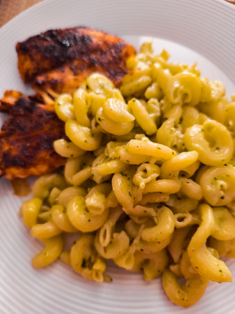Grilled chicken resting beside a hearty serving of pesto pasta creates an enticing and flavorful meal, beautifully arranged on a pristine white plate, inviting indulgenceの写真素材