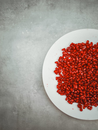 Fresh pomegranate seeds are beautifully arranged on a white plate, symbolizing the themes of rosh hashanah, rebirth, abundance, and love, set against a textured gray background with copy spaceの写真素材
