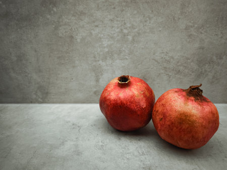 Two ripe pomegranates rest on a simple gray surface, embodying the spirit of rosh hashanah, love, and rebirth, with a focus on their rich color and symbolic meaningの写真素材