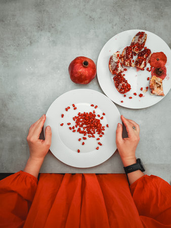 Woman in a vibrant orange dress, symbolizing joy and prosperity, holding a white plate of fresh pomegranate seeds, celebrating rosh hashanah and new beginningsの写真素材