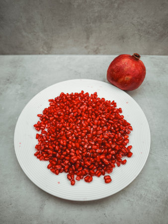 Fresh pomegranate seeds beautifully arranged on a white plate, accompanied by a whole pomegranate, representing rosh hashanah, love, rebirth, and a sense of abundanceの写真素材