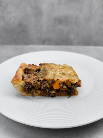 Golden brown meat pie with carrots, herbs, and melted cheese resting on a white plate, offering a savory and comforting culinary experienceの写真素材