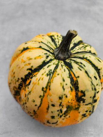 A winter squash with a creamy texture and a sweet, nutty flavor, rests on a gray surface, showing its vibrant yellow, orange, and green stripesの写真素材