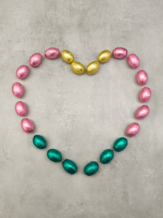 Chocolate easter eggs forming a heart shape on a grey background