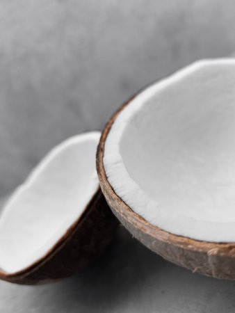 Two halves of fresh coconut resting on gray surface. Copy space, banner