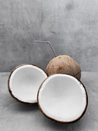 Fresh coconut showing white flesh with straw on grey background. Copy space, banner