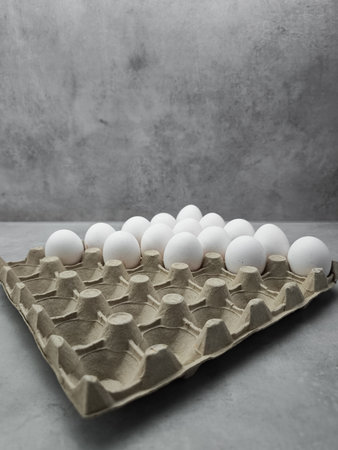 White eggs filling half cardboard container on gray background