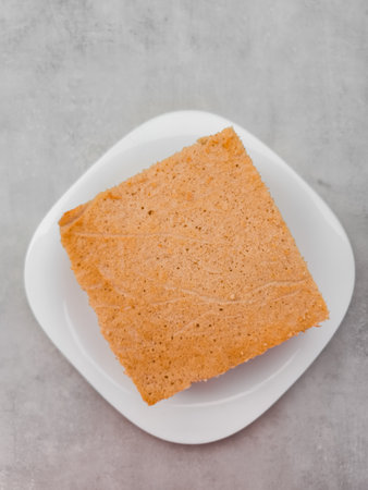 Square slice of sponge cake on white plate on marble tableの写真素材
