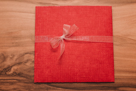 Red wedding invitation envelope with white ribbon bow on wooden tableの写真素材