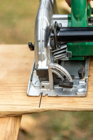 Working with a power tool. A builder is sawing a board at the construction site of a wooden benchの写真素材