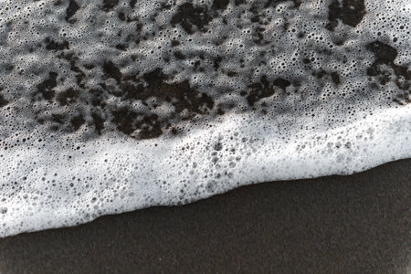 A wave runs aground on a brown sand beach. The foam of a wave comes to dry in the brown sand of a beach.の写真素材
