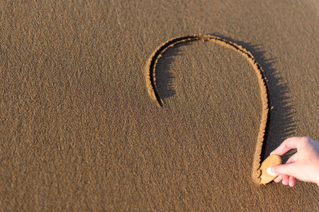 Young woman on the beach is drawing a heart shape on the sand at sunset.の写真素材