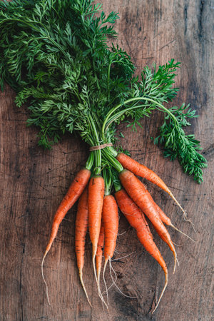 Orange carrots on a wooden background. Bunch of organic dirty fresh carrots with greens close up.