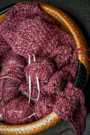 yarns, knitting needles and pattern sample in basket on sofa. closeup