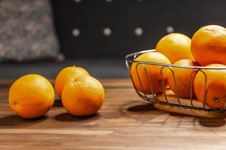 ripe unpeeled oranges in a fruit basket on a brown wooden tableの写真素材