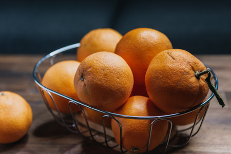 ripe unpeeled oranges in a fruit basket on a brown wooden tableの写真素材