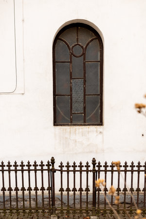 vintage brown wooden window in white wall of old church, fence