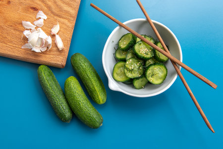 Thinly sliced cucumber salad garnished with fresh dill and sesame seeds, served in a white bowl on a blue background. Light, healthy, and refreshing dish. Japanese cucumber saladの写真素材