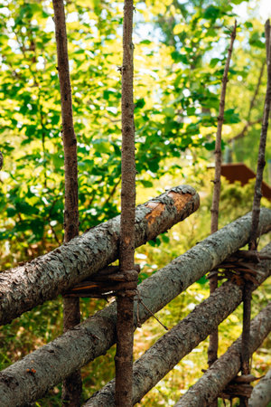 Close-up of a rustic Swedish wooden fence made of logs and twine in a sunlit green forest. Traditional Scandinavian craftsmanship in nature.の写真素材