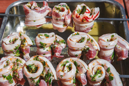 Close-up of raw marinated pork belly skewers with fresh herbs and spices, ready for barbecue grilling. Traditional outdoor cooking and meat preparation concept.の写真素材
