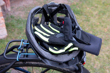 A pair of black and neon yellow cycling gloves placed inside a bicycle helmet, resting on the rear rack of a bike outdoors.の写真素材