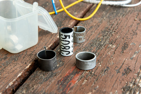 Close-up of bird ringing tools on a wooden table, including colored wires and numbered metal bands...
