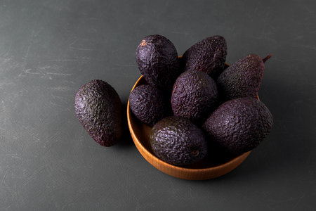Dark, ripe avocados in wooden bowl on a rustic green surface, captured in soft moody lighting.の写真素材