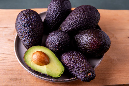 Dark, ripe avocados on a wooden cutting board, captured in soft moody lighting.の写真素材