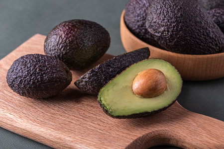 Dark, ripe avocados on a wooden cutting board on a rustic green surface, captured in soft moody...