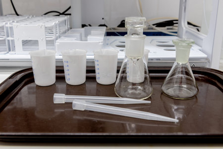 Laboratory equipment. Plastic beakers, glass flasks, pipette tips on plastic brown tray.