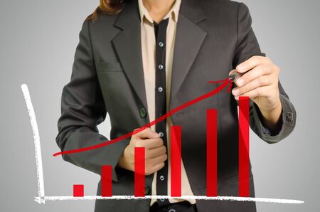 Business woman pointing rising red chart on gray background.の写真素材