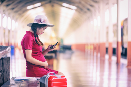 Pregnant woman tourist  with look searching direction on location phone with tourists bag or luggage while traveling by train. Vacation conceptの写真素材