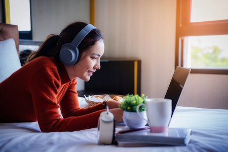 Happy beautiful young woman working in bed using laptop computer at home. lifestyle and technology at home concept.の写真素材