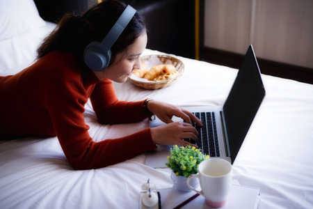 Happy beautiful young woman working in bed using laptop computer at home. lifestyle and technology at home concept.の写真素材
