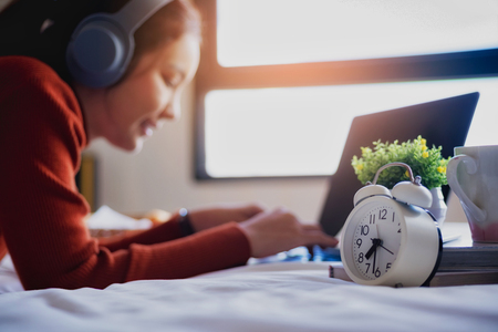 Young beautiful woman relaxing with use headphones listening to music and laptop on bed in the holiday.の写真素材
